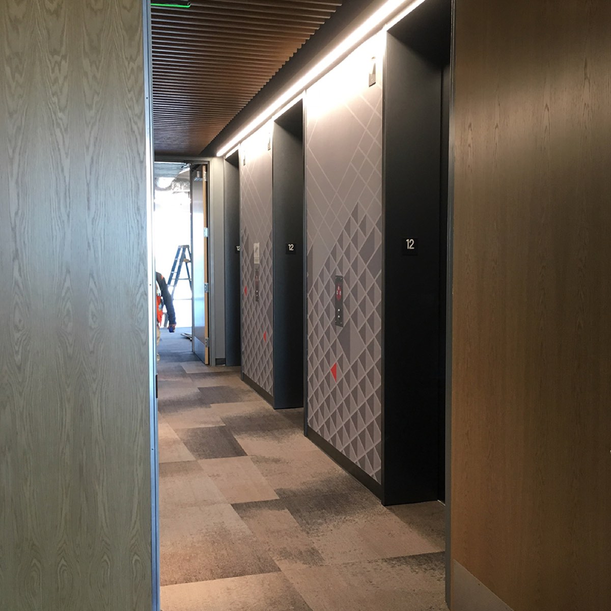 Geometric contract wallcovering across an elevator corridor, wide view, installed by Mancini Wallpapers