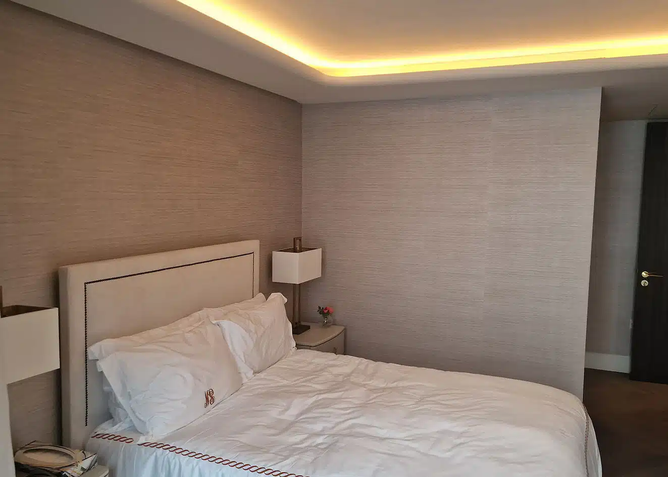 Grasscloth wallcovering across a primary bedroom with cove lighting, installed by Mancini Wallpapers, Park City, Utah