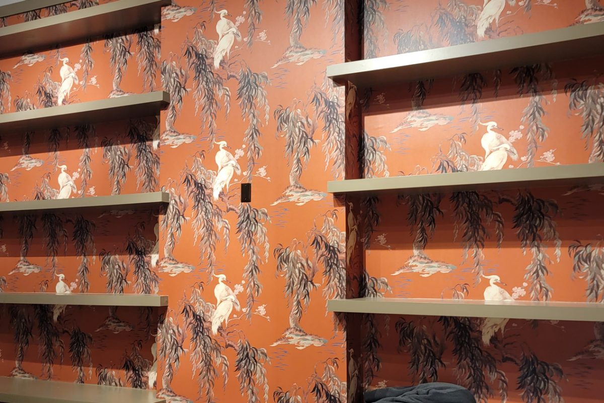Orange chinoiserie wallpaper behind closet shelving, installed by Mancini Wallpapers